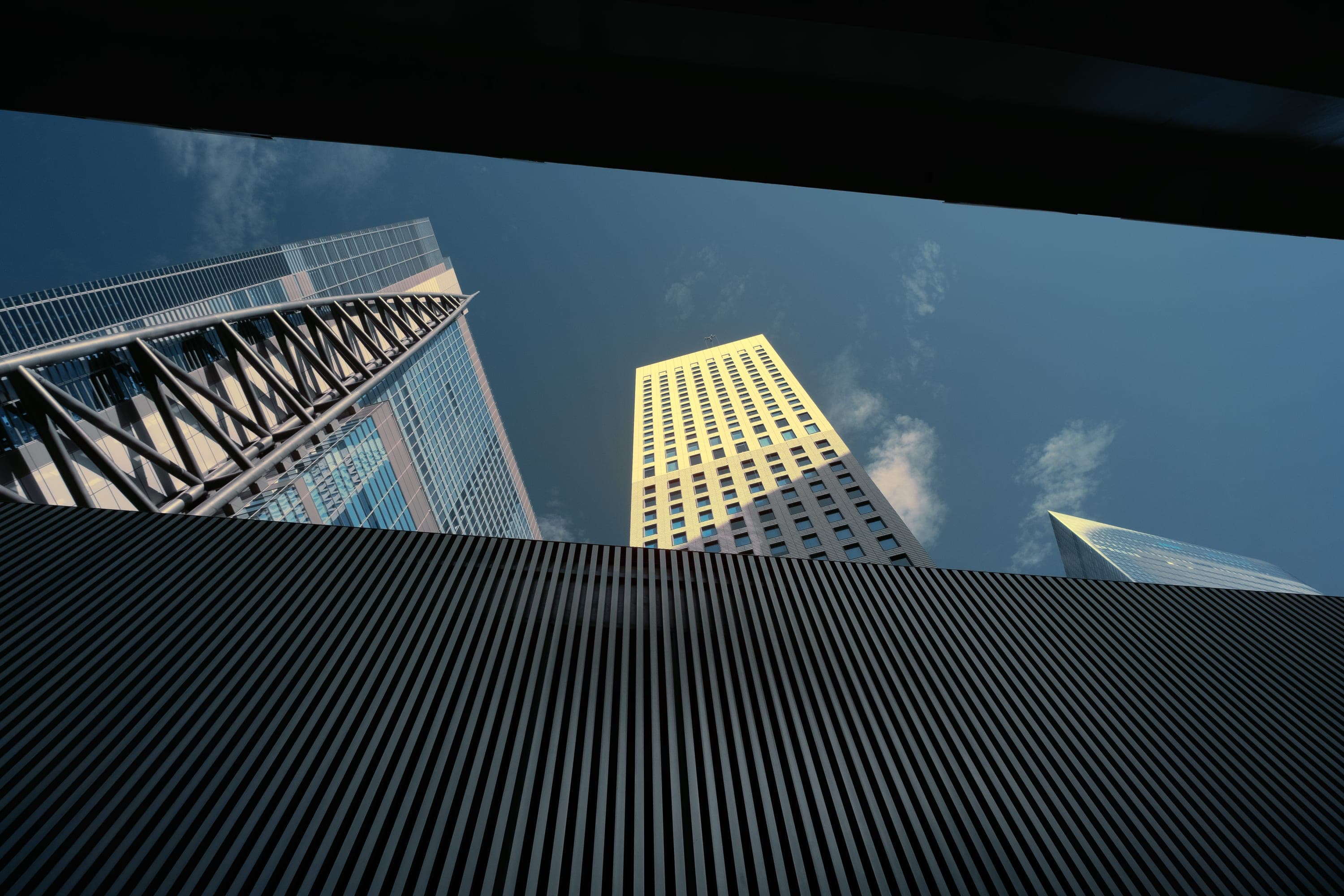 A gold-lit skyscraper flanked by black ribbed facades against deep blue sky