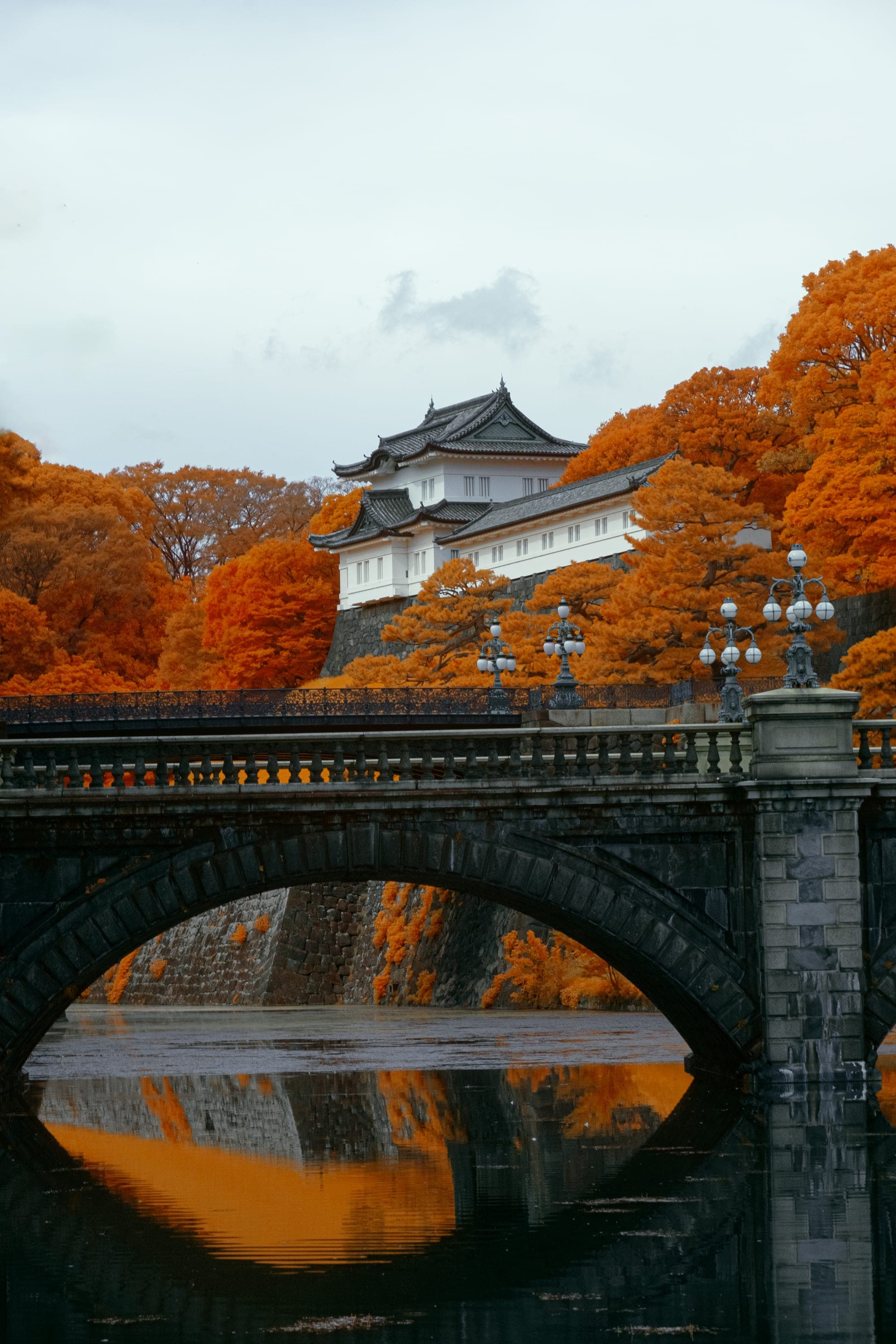 A stone arch bridge over still moat water, a white keep rising from autumn-orange trees