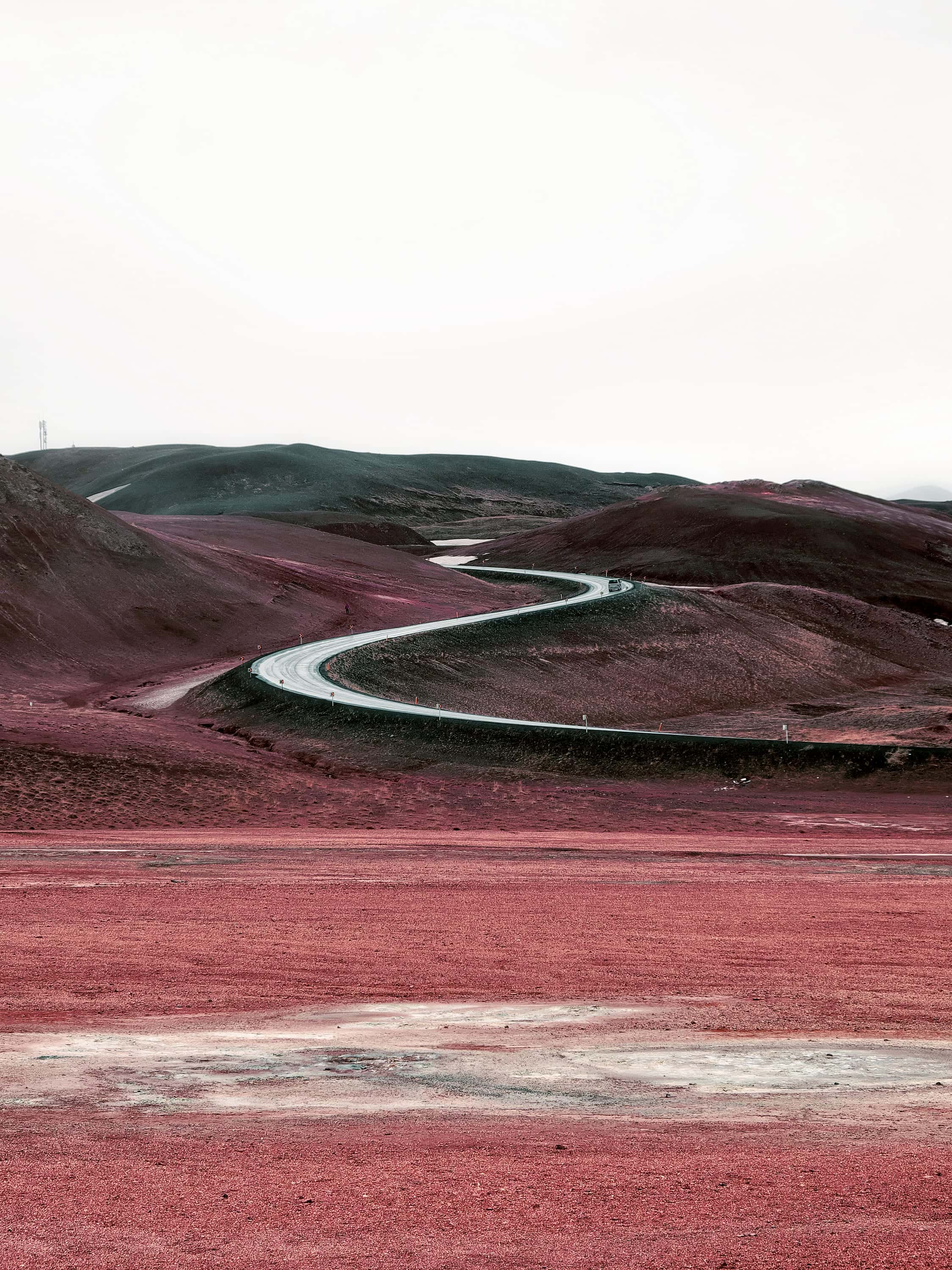 A gravel road winding through a valley floor of dusty red ground toward pale hills