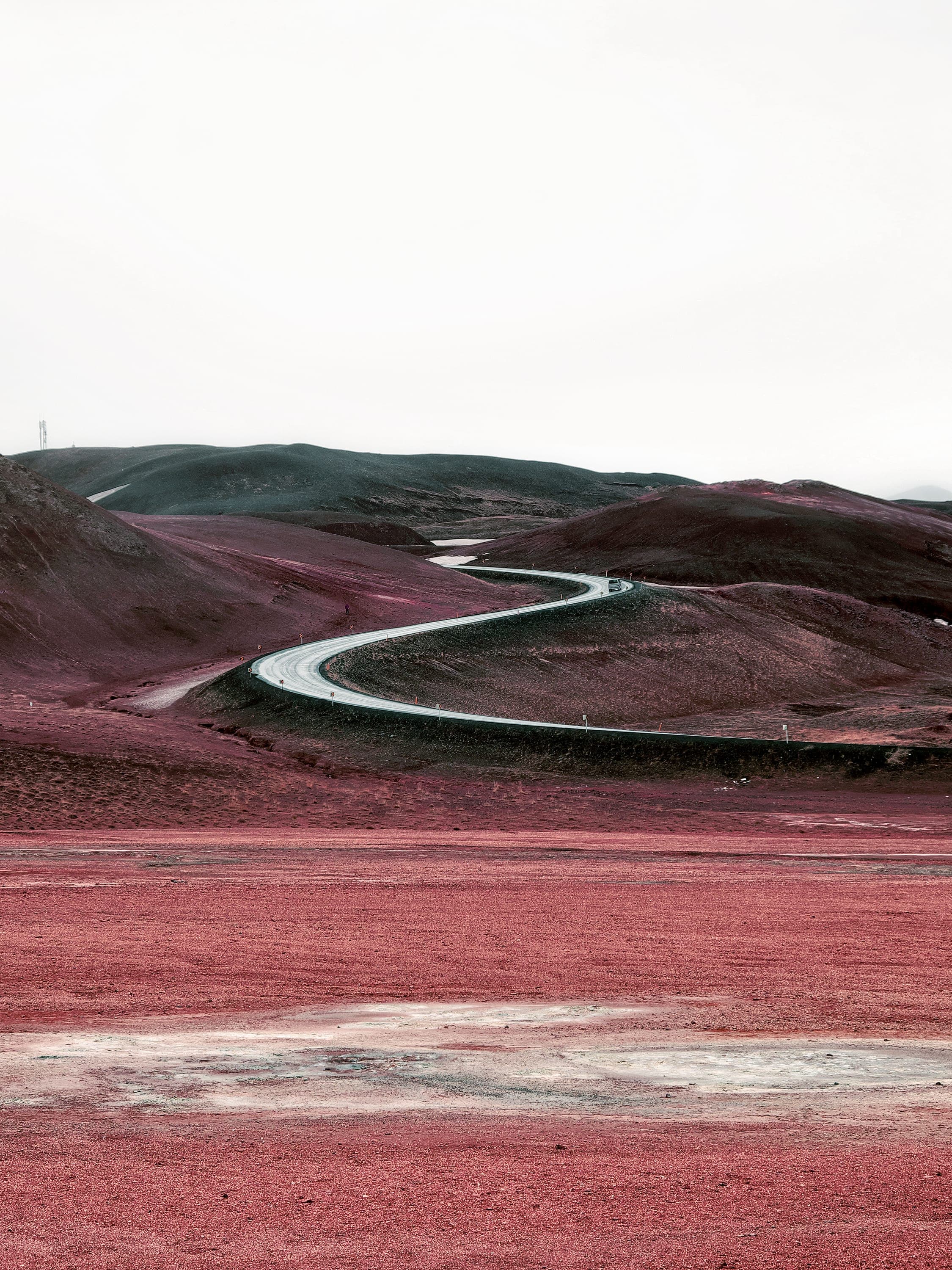 A gravel road winding through a valley floor of dusty red ground toward pale hills