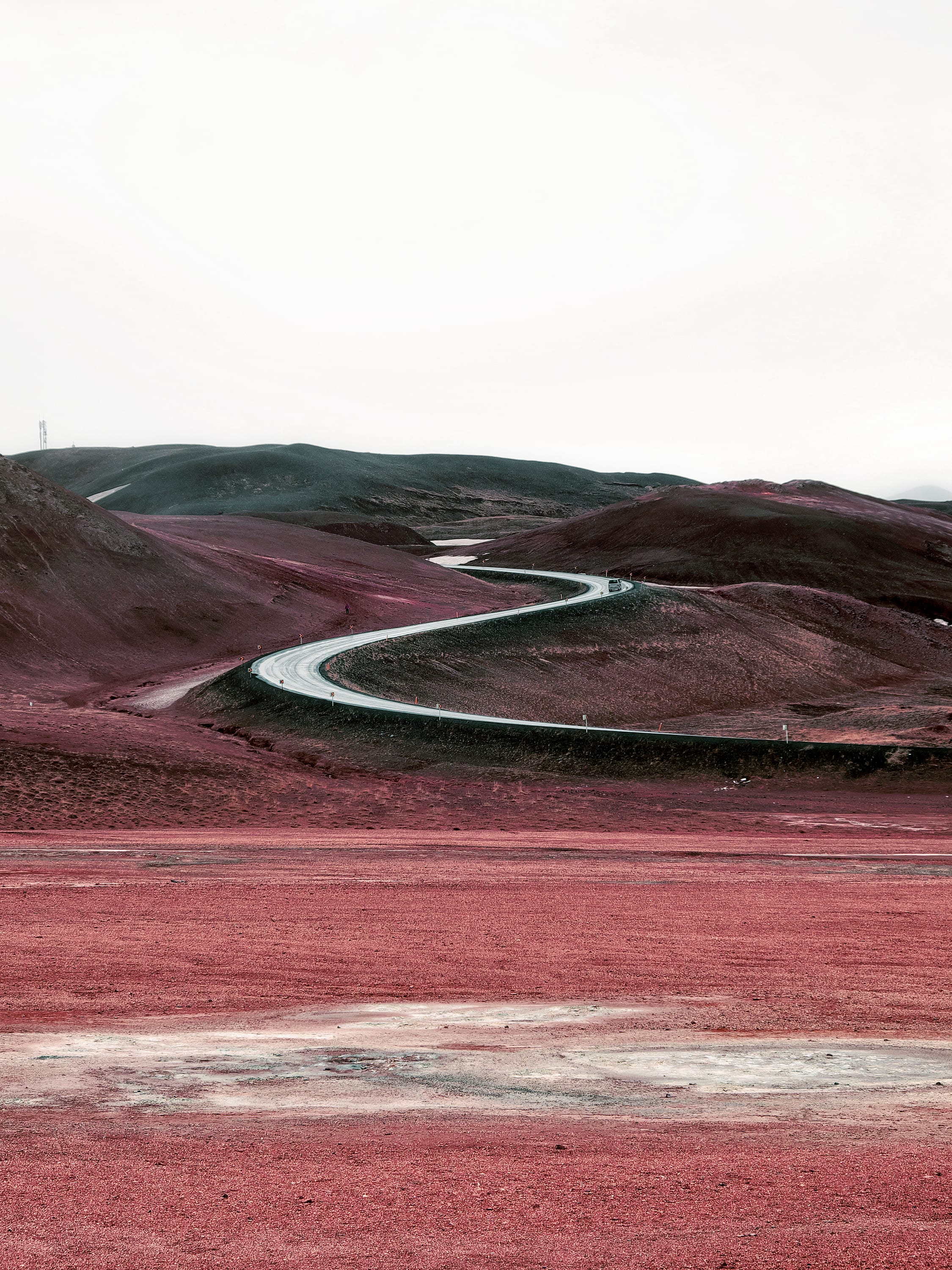 A gravel road winding through a valley floor of dusty red ground toward pale hills