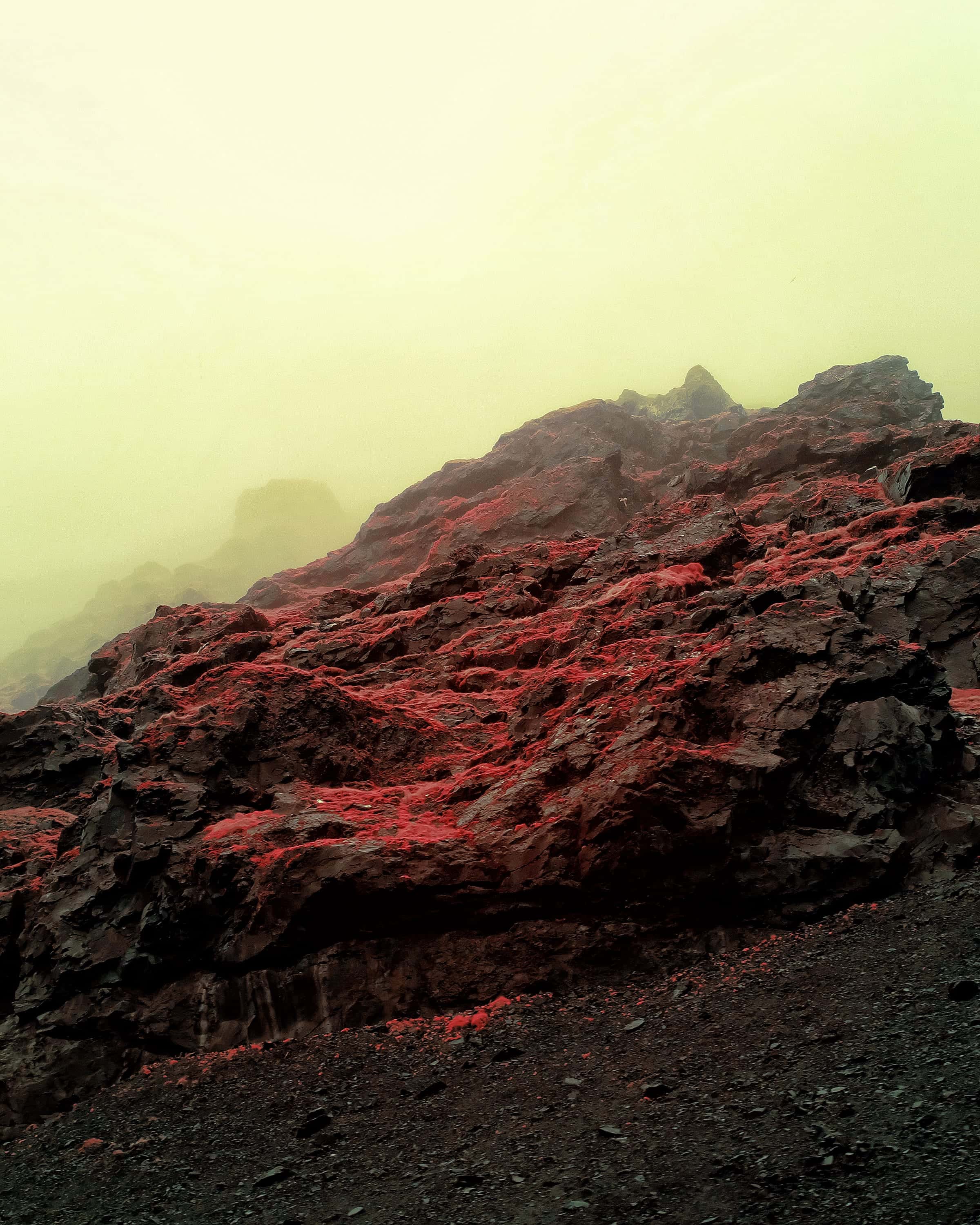 A dark ridgeline of red scree dissolving upward into yellow-green fog