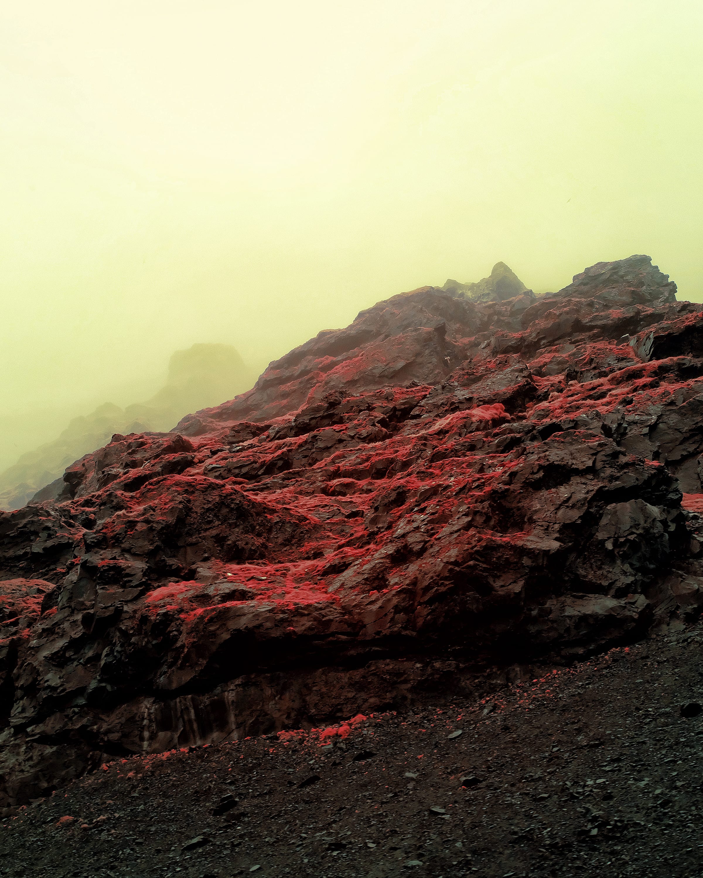 A dark ridgeline of red scree dissolving upward into yellow-green fog