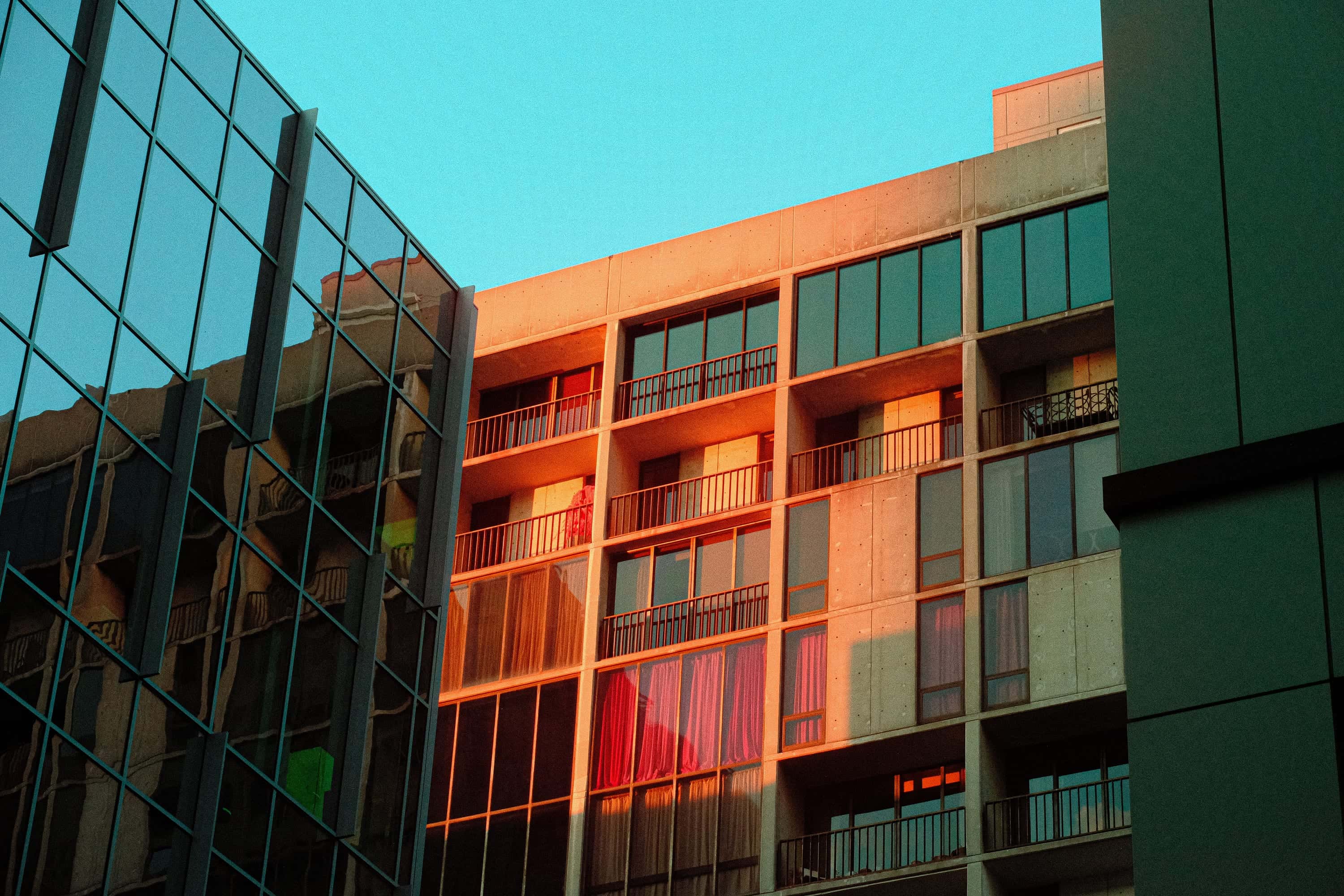 Late sun raking an apartment facade in orange behind a green glass curtain wall