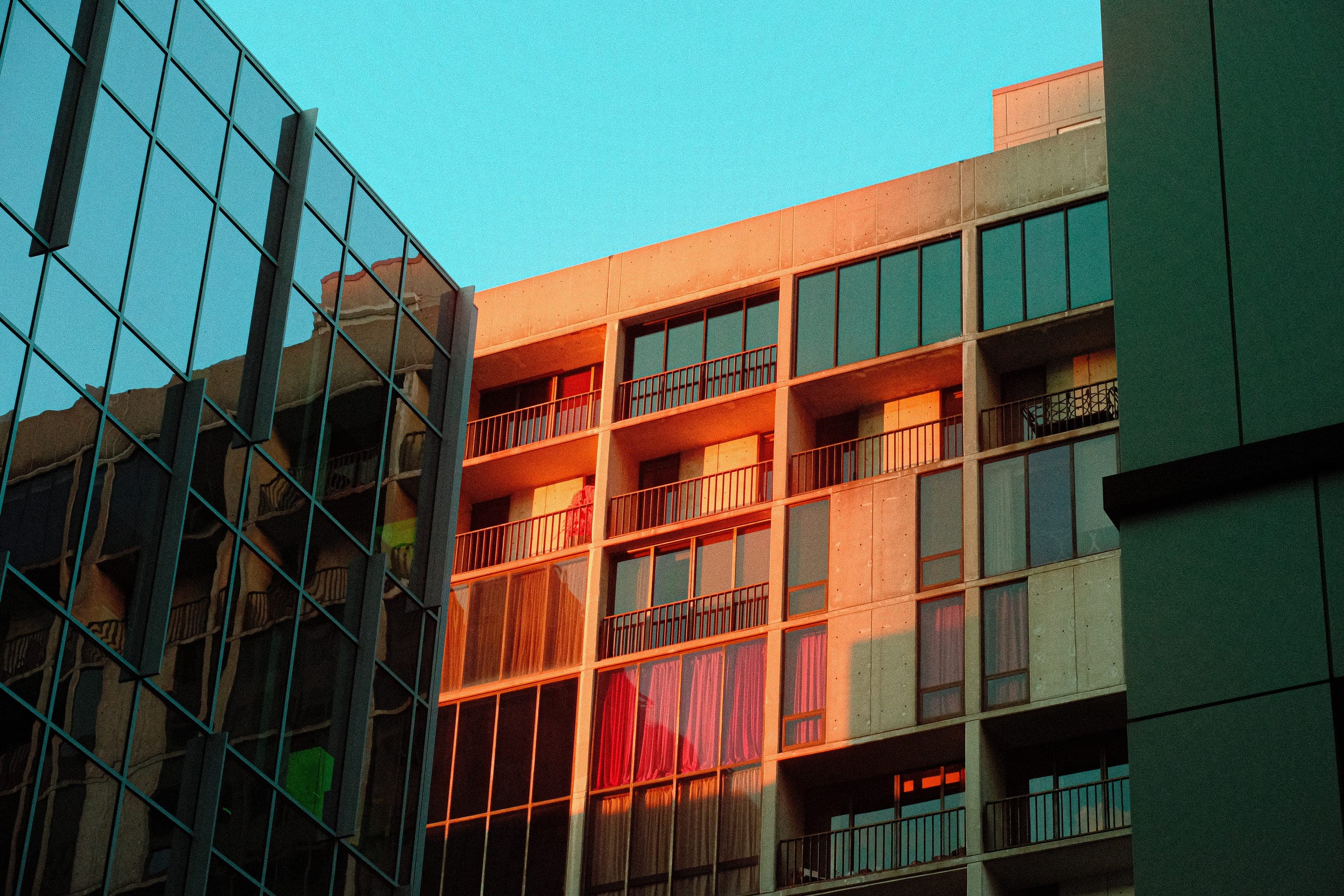 Late sun raking an apartment facade in orange behind a green glass curtain wall