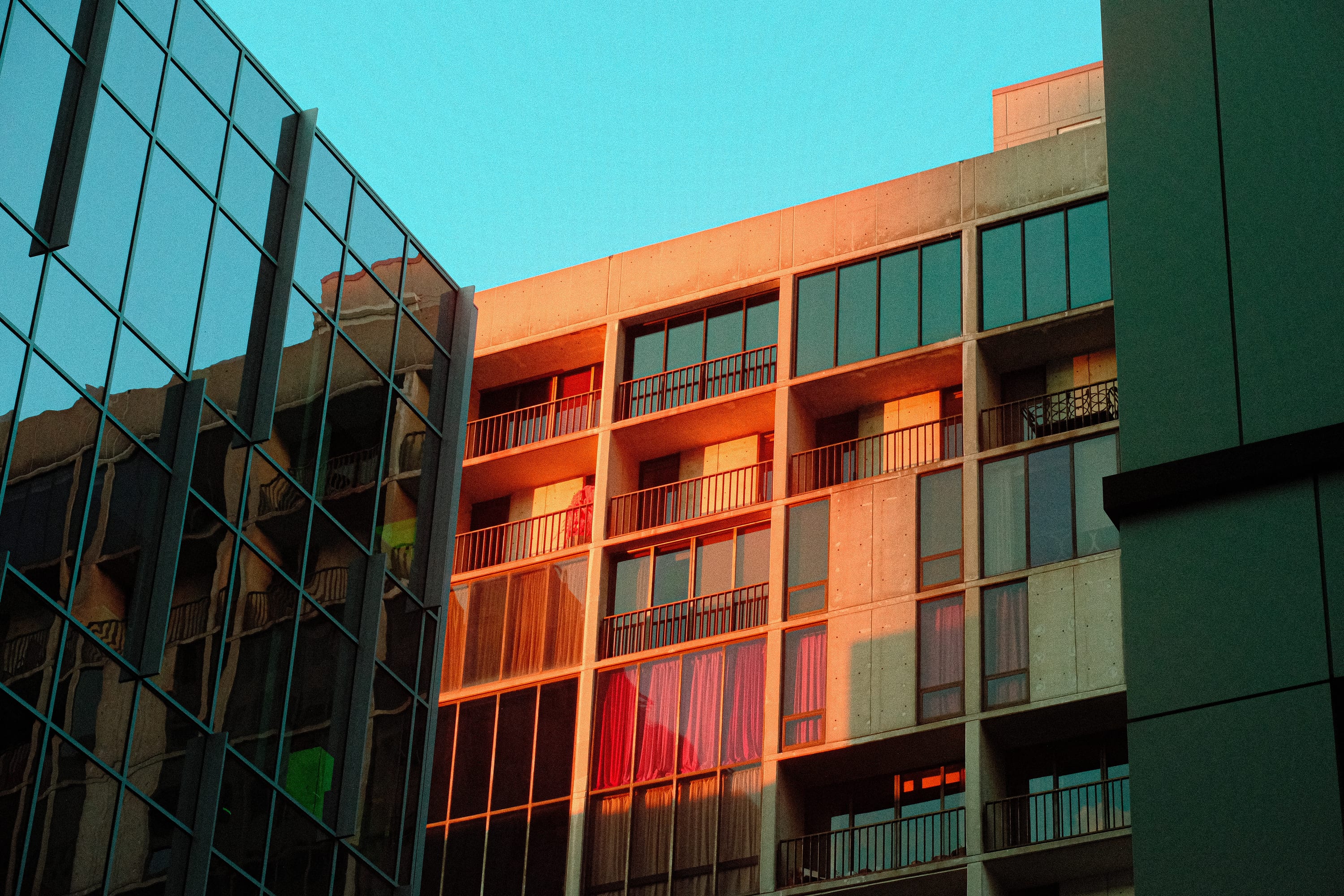 Late sun raking an apartment facade in orange behind a green glass curtain wall