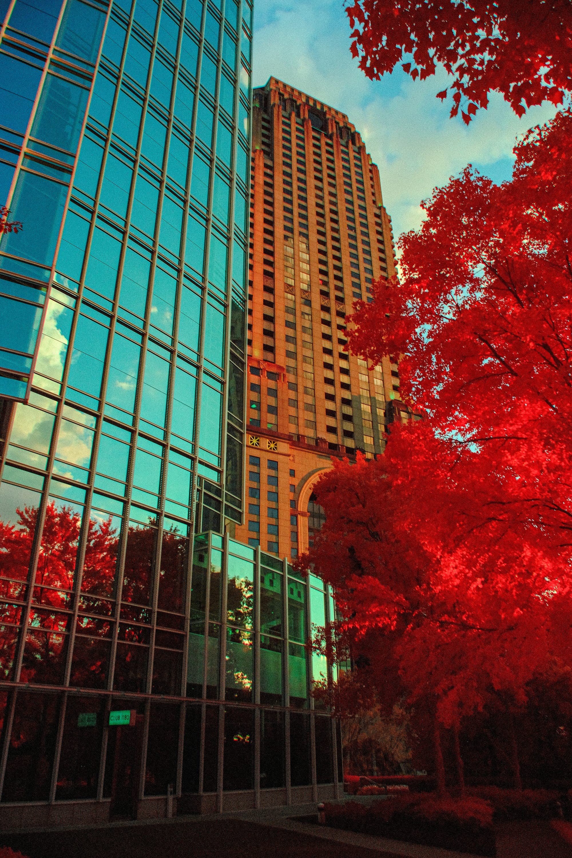 A reflective tower rising past crimson canopy from a paved court, seen from below